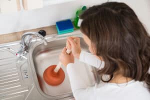 Woman using plunger to clear a kitchen sink clog